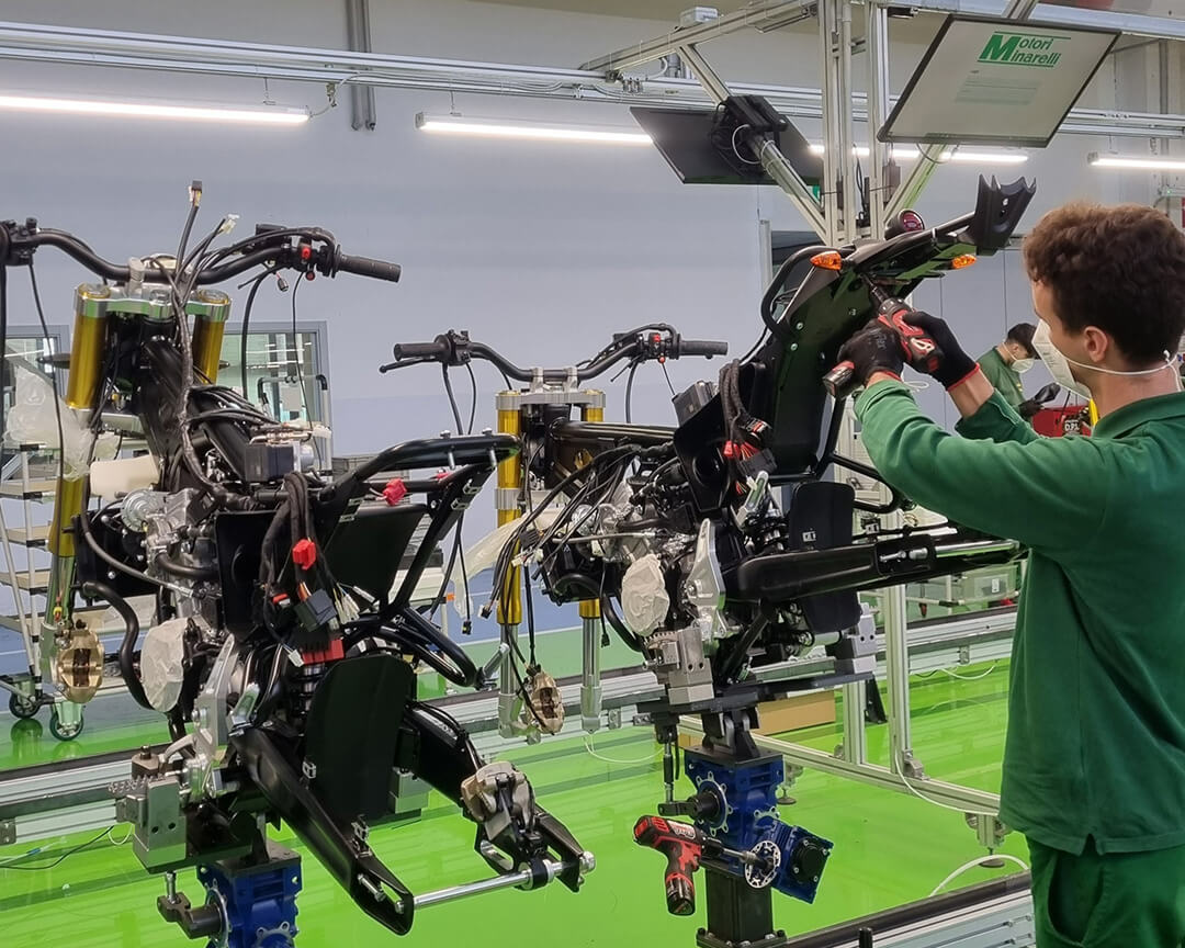 Inside the assembly line in the Minarelli factory, a mechanic screws a motorcycle tail part with a drill