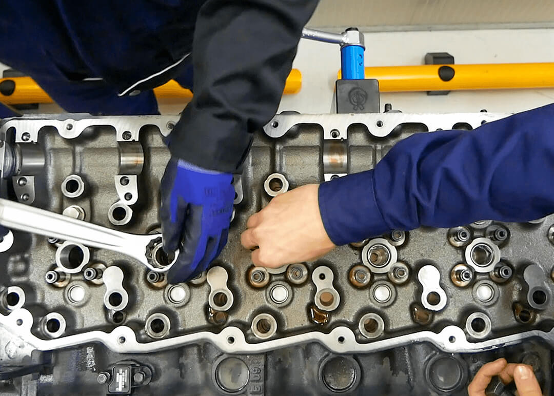 Le mani di due meccanici powertrain che lavorano sulla testata di un motore