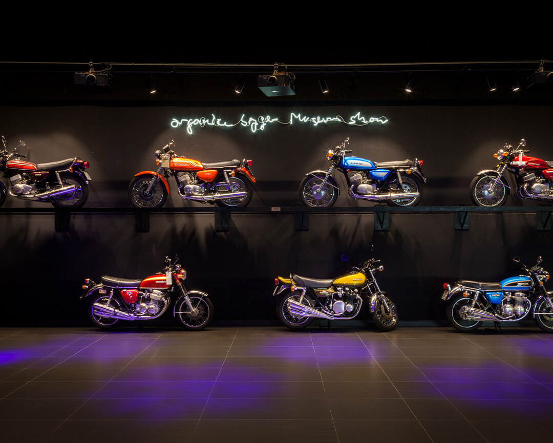 Inside an exhibition hall of Ruote da Sogno, a series of illuminated collectible motorcycles are displayed