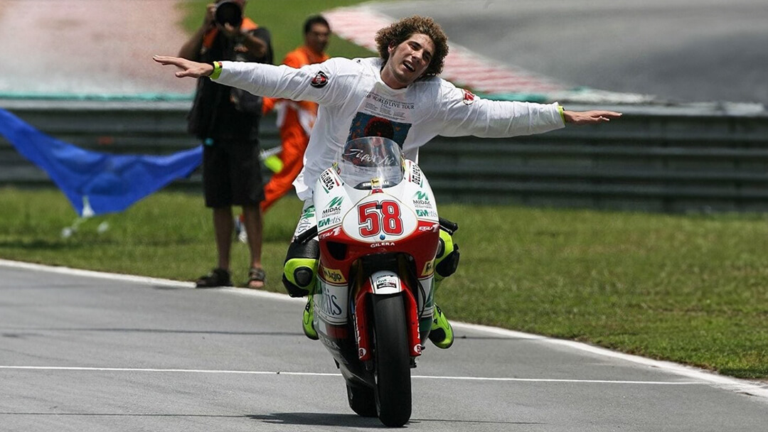 foto di marco simoncelli su moto numero 58 senza casco che sorride con braccia aperte