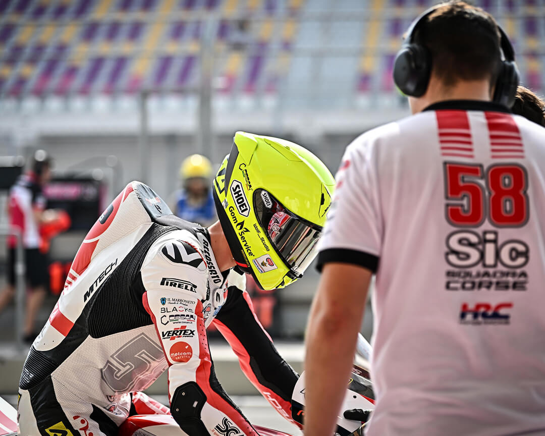 pilota con casco giallo fluo e allenatore con maglietta con la scritta SIC 58