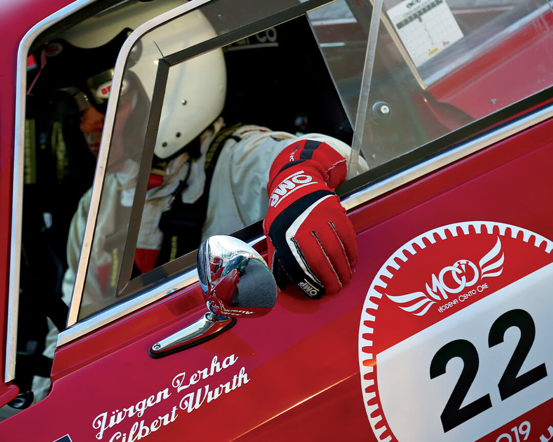 mano con guanto che esce da finestrino di auto da corsa d'epoca rossa