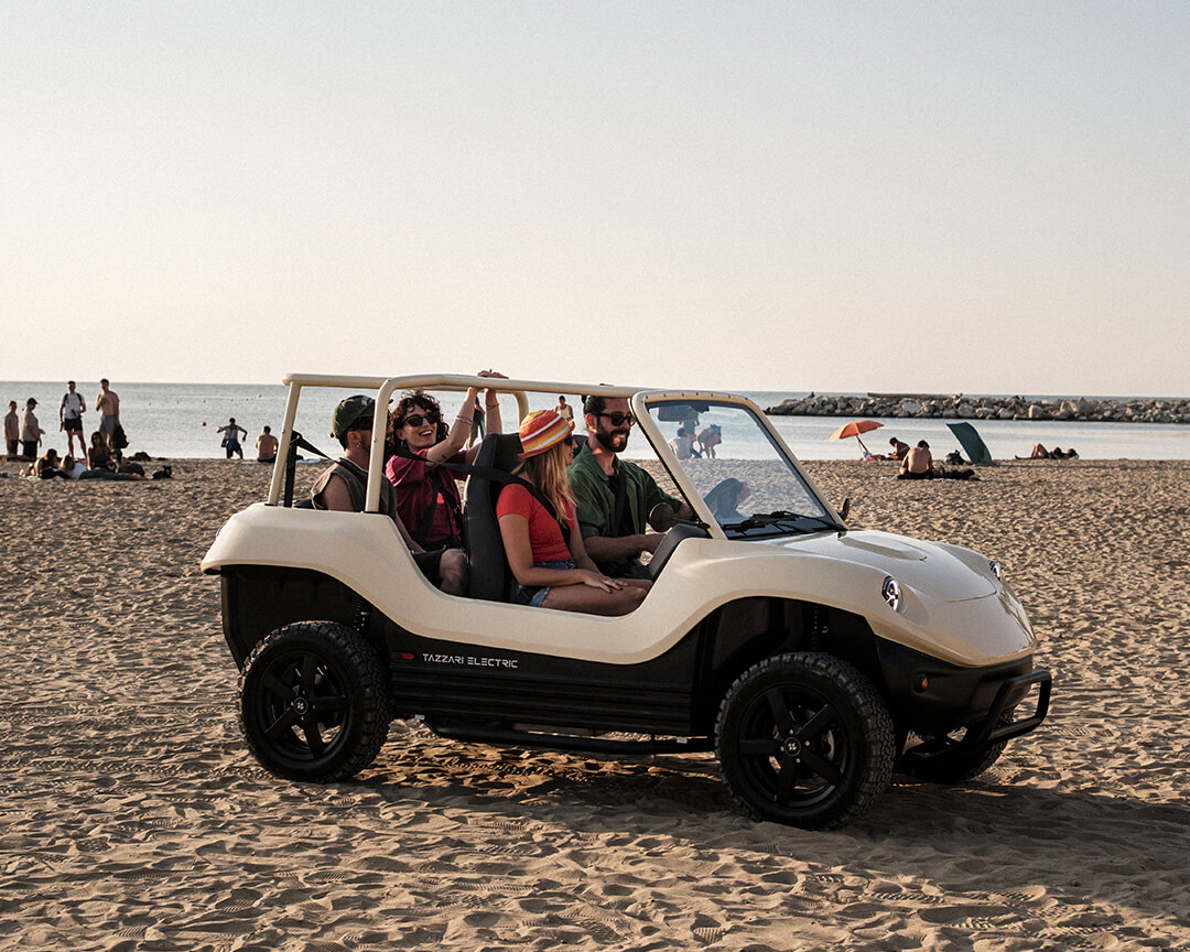 Tazzari's electric dune buggy with four people on board in the middle of a beach