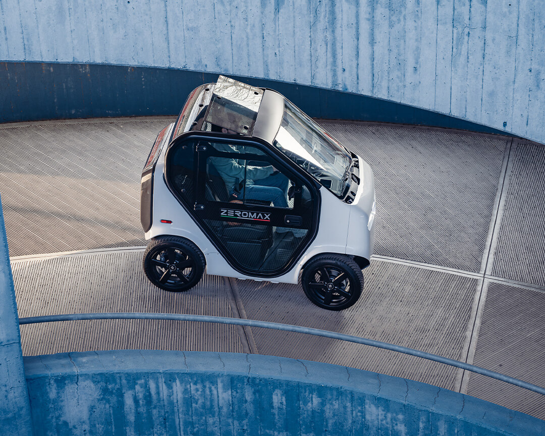 Two-seater zeromax model of tazzari driving down a winding street of a multi-story parking lot