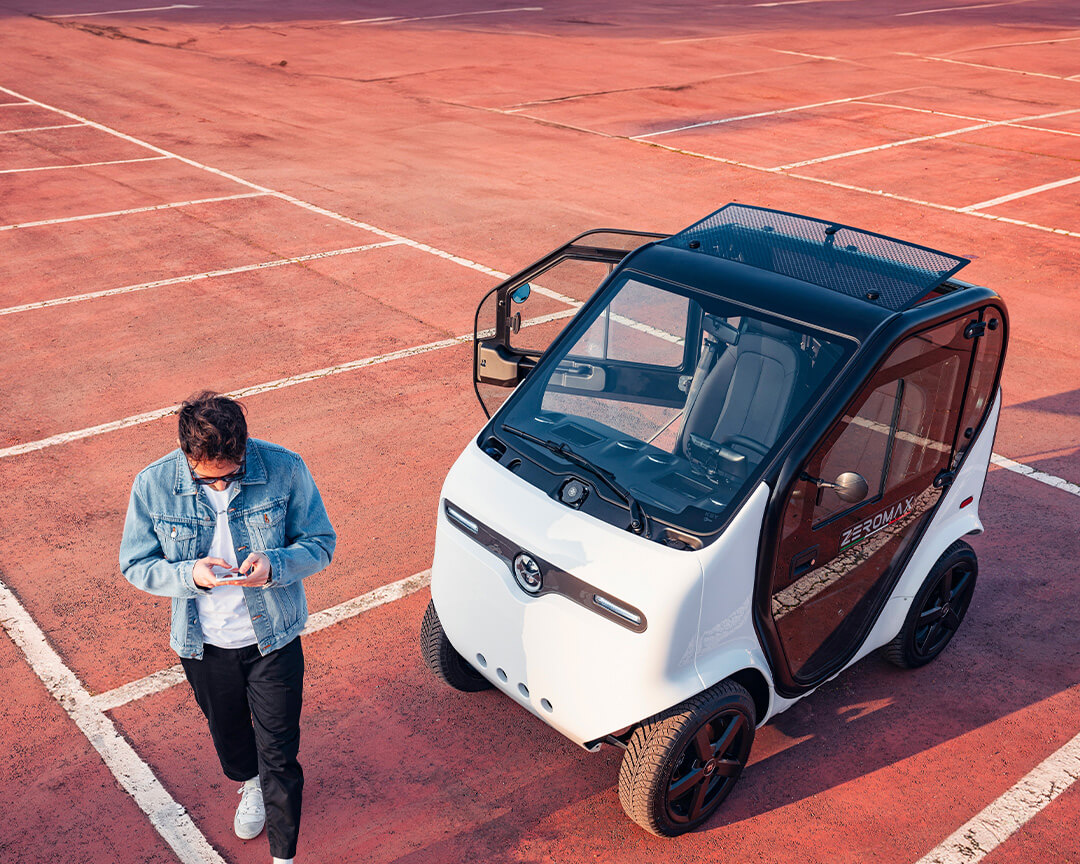 Two-seater Zeromax model by tazzari, in black and white coloring with one door and roof open, inside a parking lot
