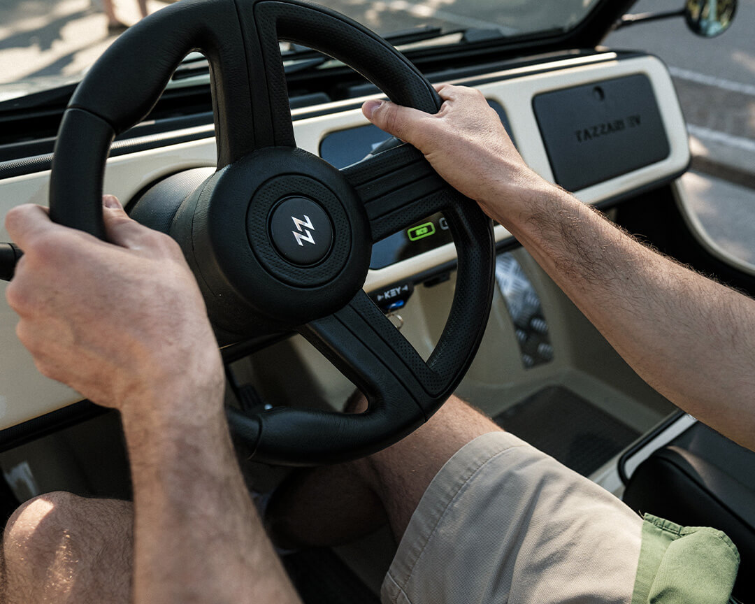 Steering wheel of a tazzari electric car , with a chrome tazzari logo in the center of the steering wheel