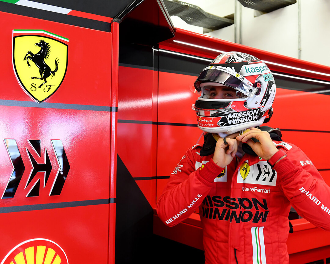 pilota Ferrari in tuta da corsa che si allaccia il casco dentro il box ferrari