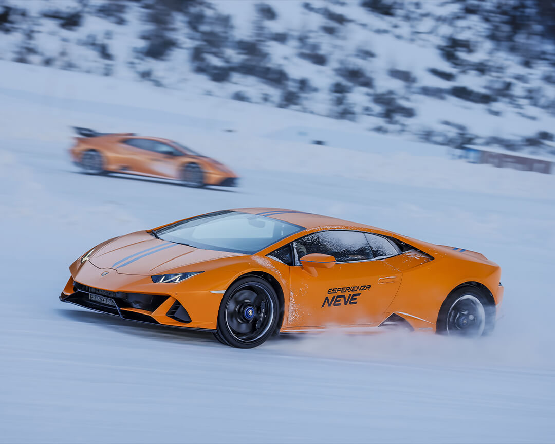 super car  Lamborghini color arancione con scritta Esperienza Neve che sfreccia sulla neve