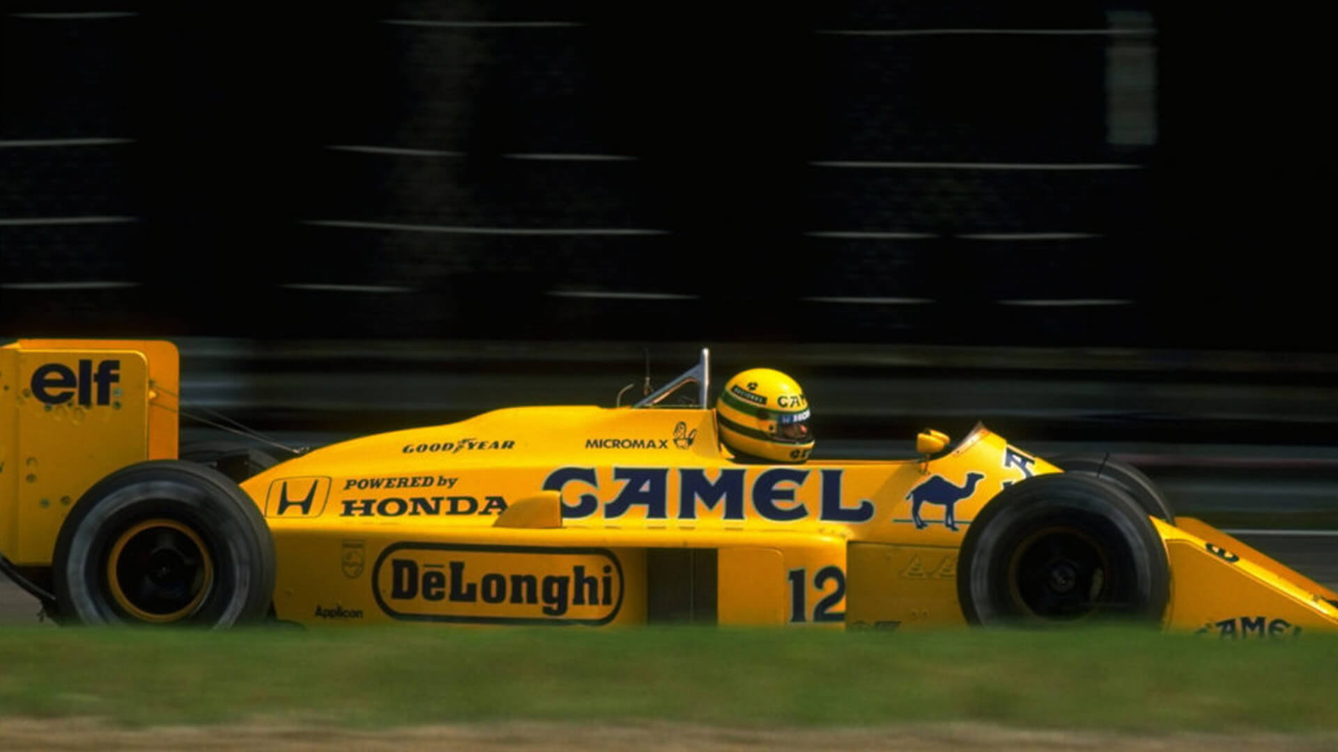 Formula 1 car of the Lotus 99T, featuring yellow livery sponsored by Camel, with driver Ayrton Senna behind the wheel.