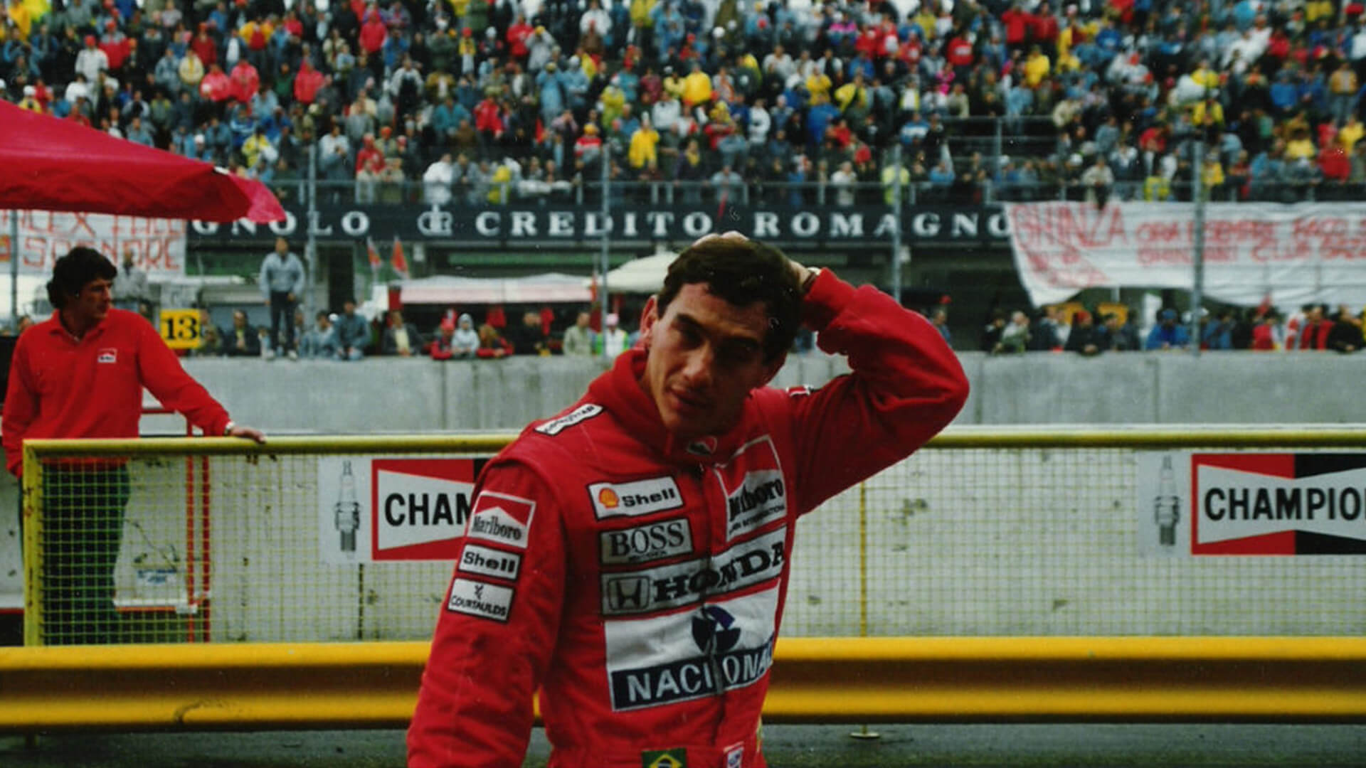 photo of Ayrton Senna after a race in red suit and behind the stands with the public