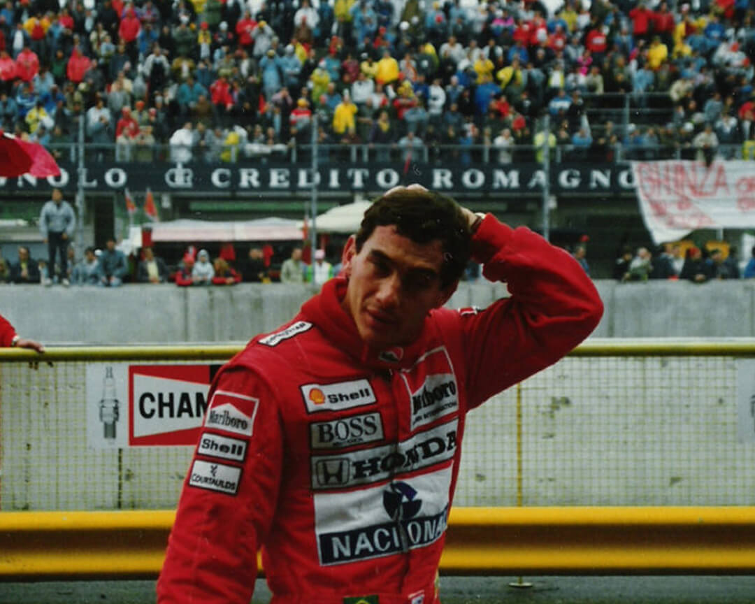 foto di Ayrton Senna dopo una gara con tuta rossa e alle spalle gli spalti con il pubblico