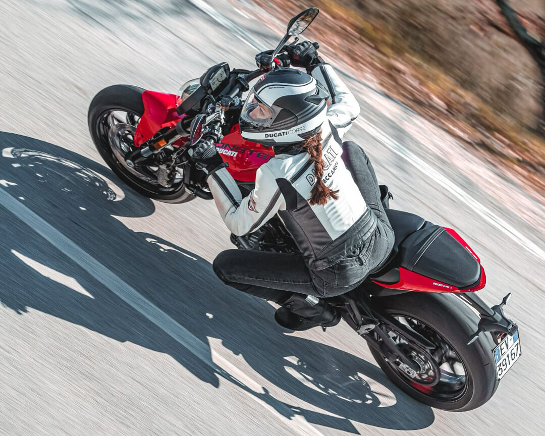 Chiara lovato who rides a monster ducati takes a curve, while wearing the technical clothing ducati corse white