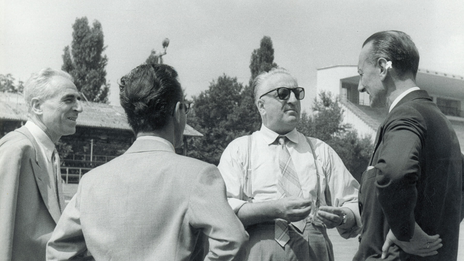 foto in bianco e nero di uomini in giacca e cravatta che ascoltano Enzo Ferrari parlare