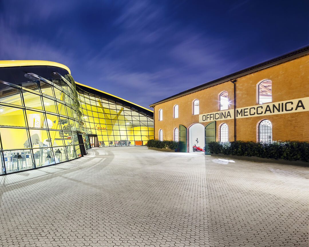 esterno del Museo Enzo Ferrari a sinistra la struttura a vetri con pareti gialle e a destra una struttura con insegna Officina Meccanica