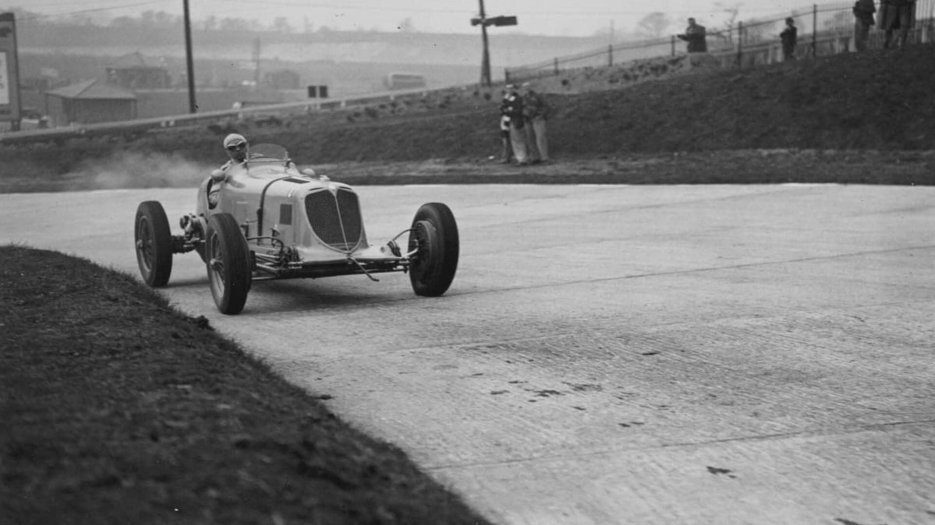 In una foto antica in bianco e nero viene ritratta una maserati d'epoca mentre affronta una curva di un tracciato