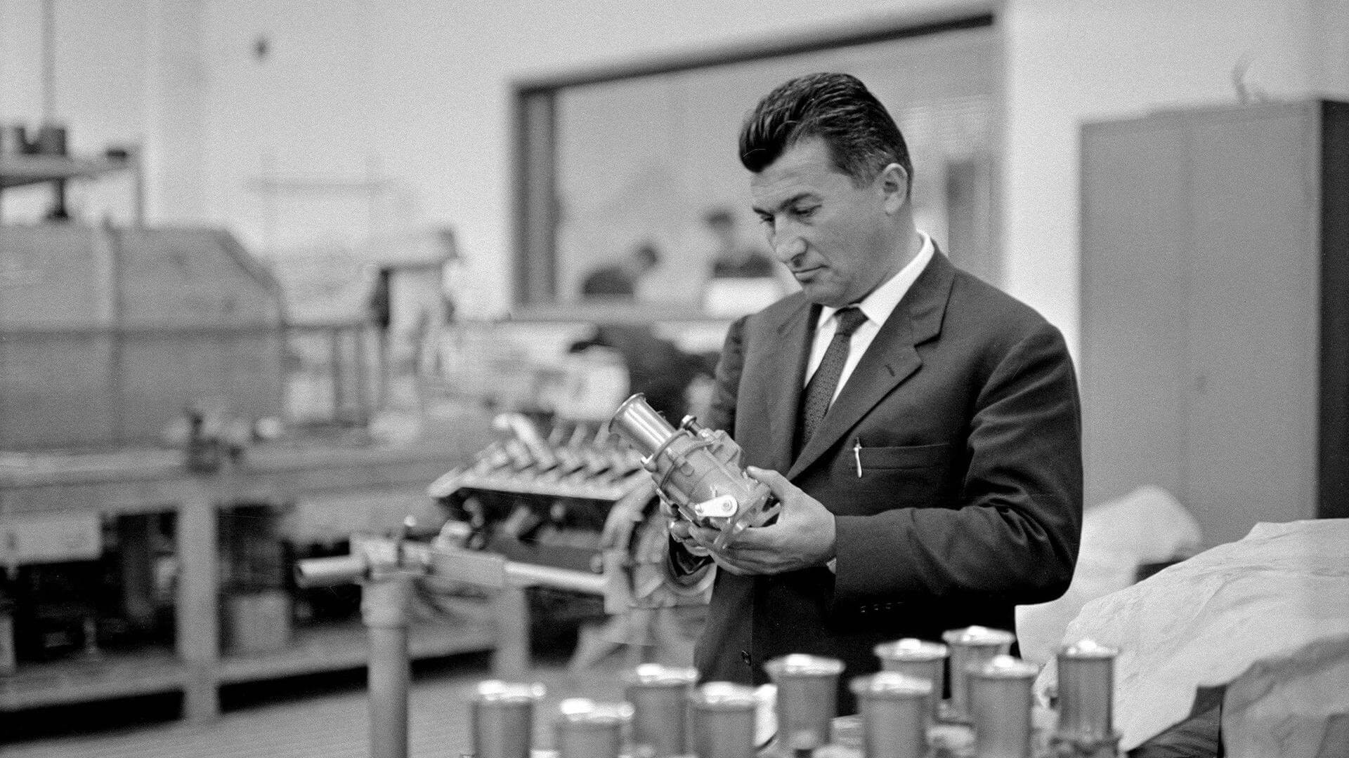 In una vecchia foto in bianco e nero ferruccio lamborghini osserva una componente meccanica di una delle sue vetture