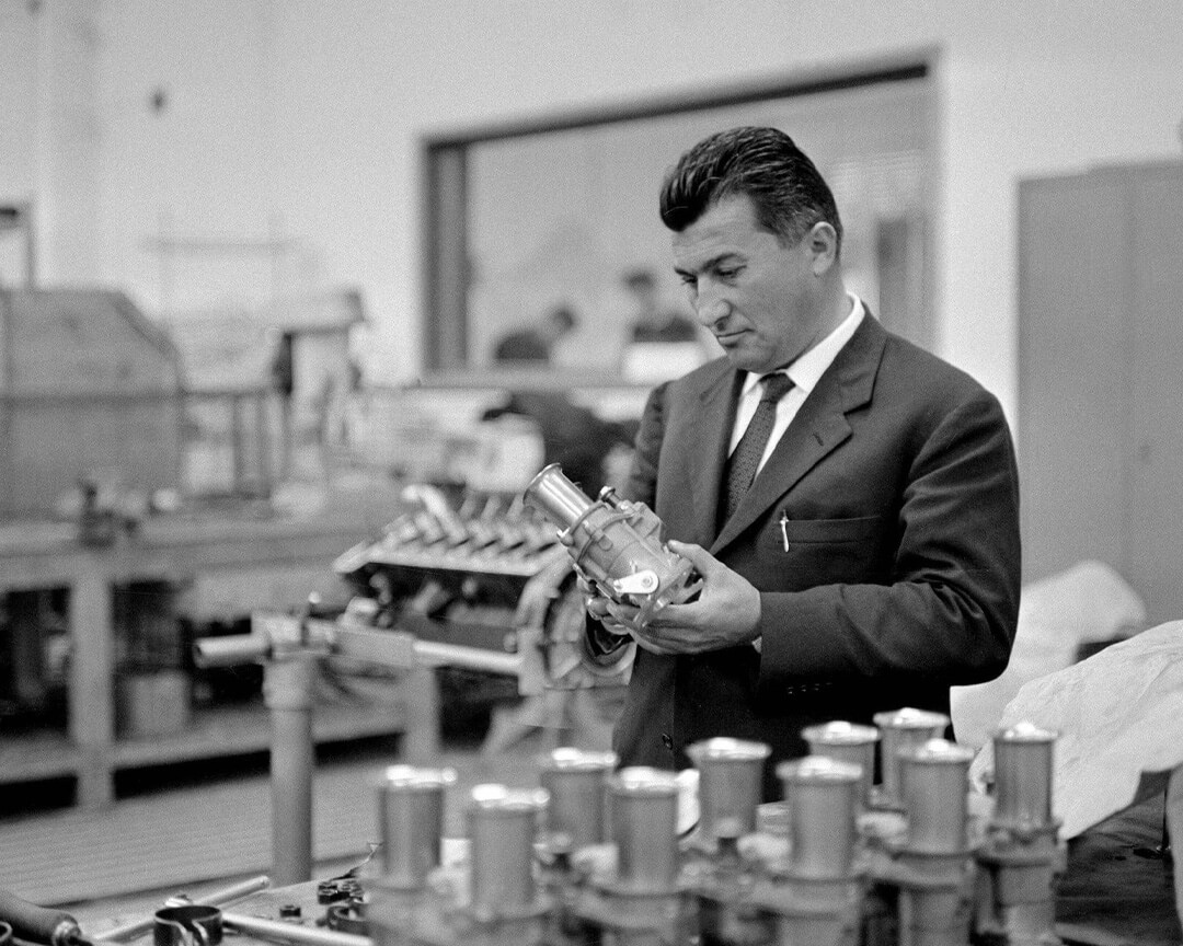 In una vecchia foto in bianco e nero ferruccio lamborghini osserva una componente meccanica di una delle sue vetture