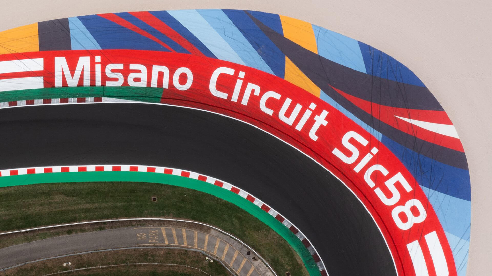 foto dall'alto del circuito di Misano con scritta bianca Misano Circuit Sic58 su sfondo rosso e disengi colorati