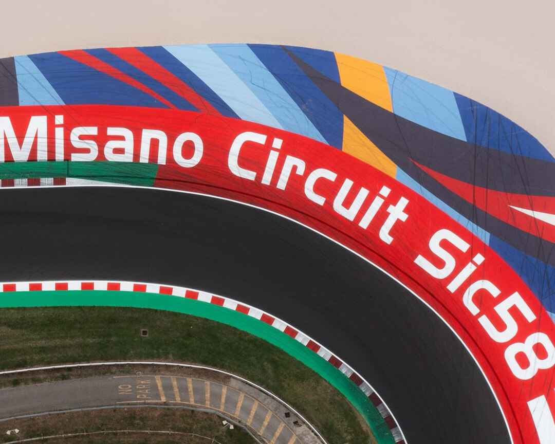 foto dall'alto del circuito di Misano con scritta bianca Misano Circuit Sic58 su sfondo rosso e disengi colorati