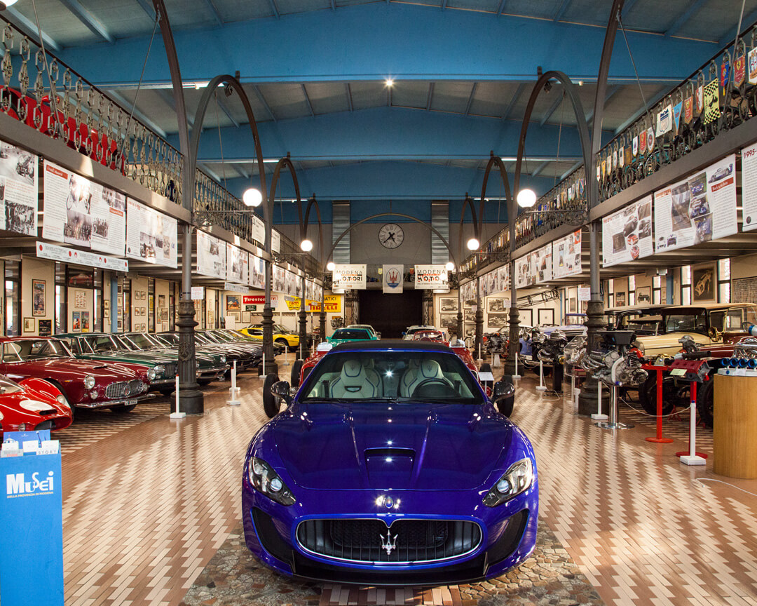 Foto frontale di una sala espositiva della collezione panini, con in primo piano una maserati gran turismo blu, e ai lati molte altre maserati storiche