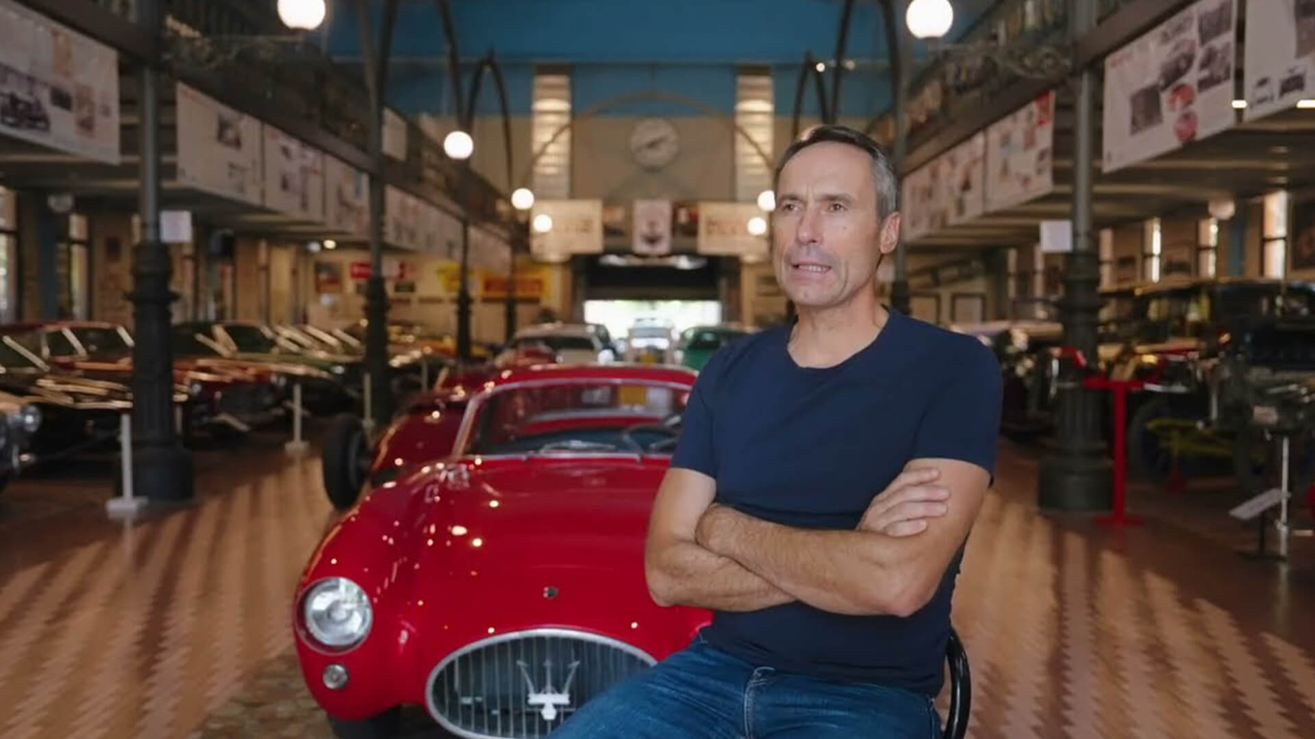 Umberto panini seduto davanti ad una maserati della sua collezione mentre viene intervistato