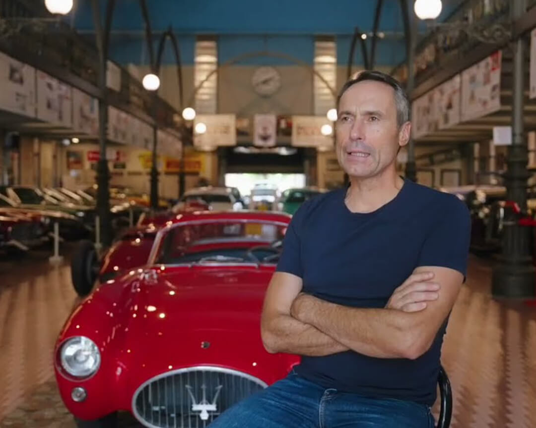 Umberto panini seduto davanti ad una maserati della sua collezione mentre viene intervistato