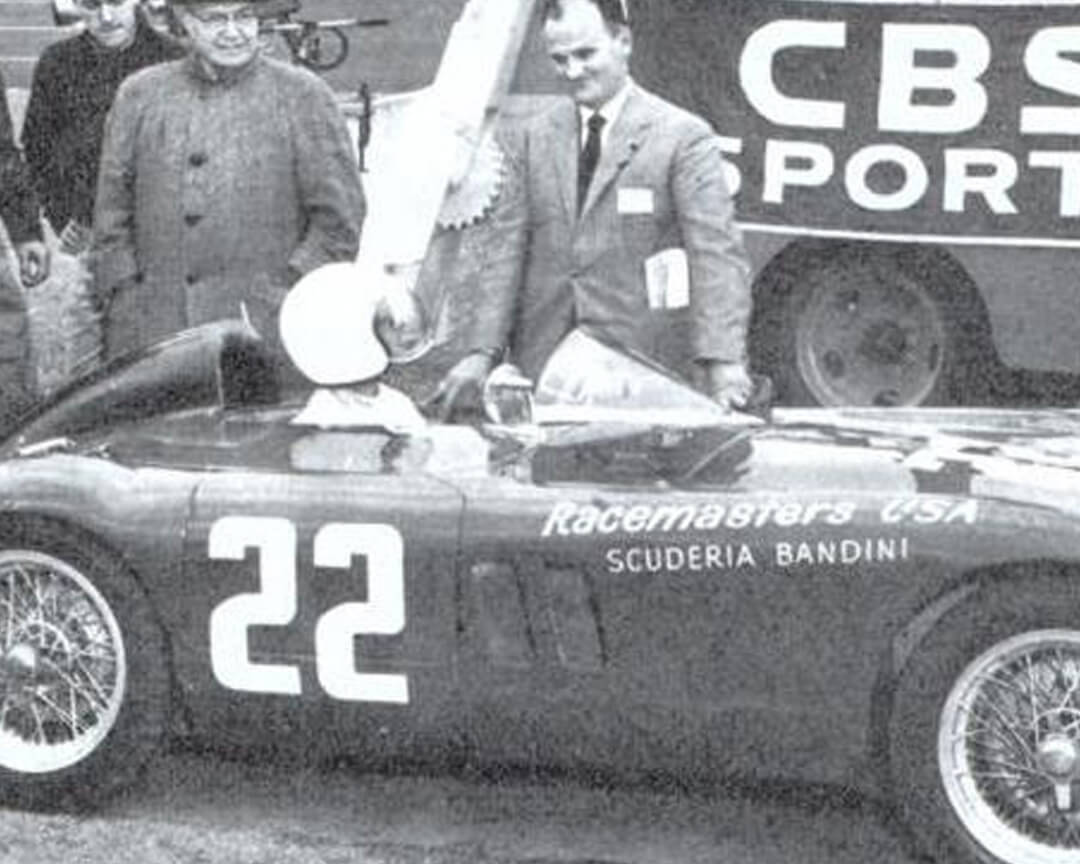 foto in bianco e nero di Ilario Bandini alla guida di una Bandini 750 Sport Internazionale, la "Saponetta", con il numero 22 e il direttore di gara in piedi