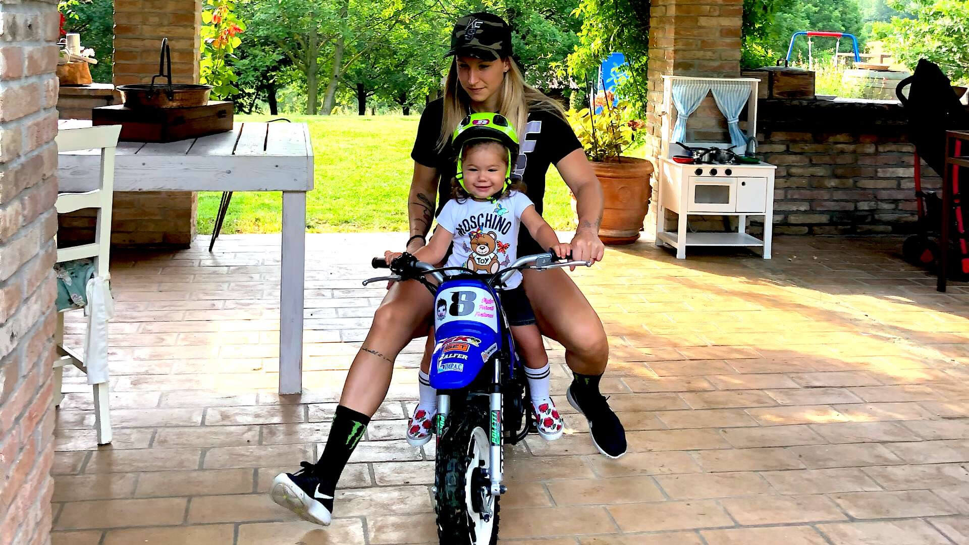 Kiara Fontanesi riding a minimoto takes a ride in the garden with her young daughter
