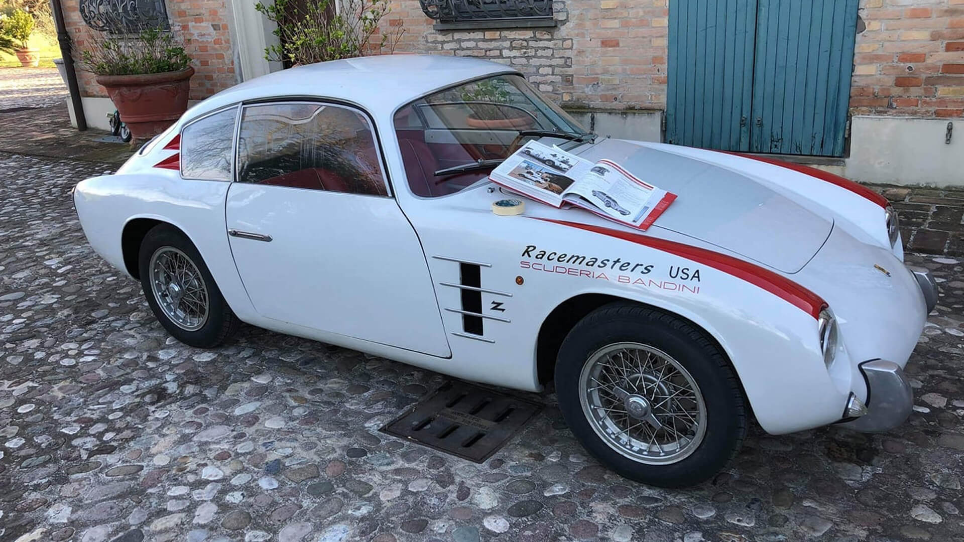 foto di Bandini GT 750 con dettagli rossi e la scritta scuderia bandini con libro di auto adagiato sopra e rotolo di scotch carta
