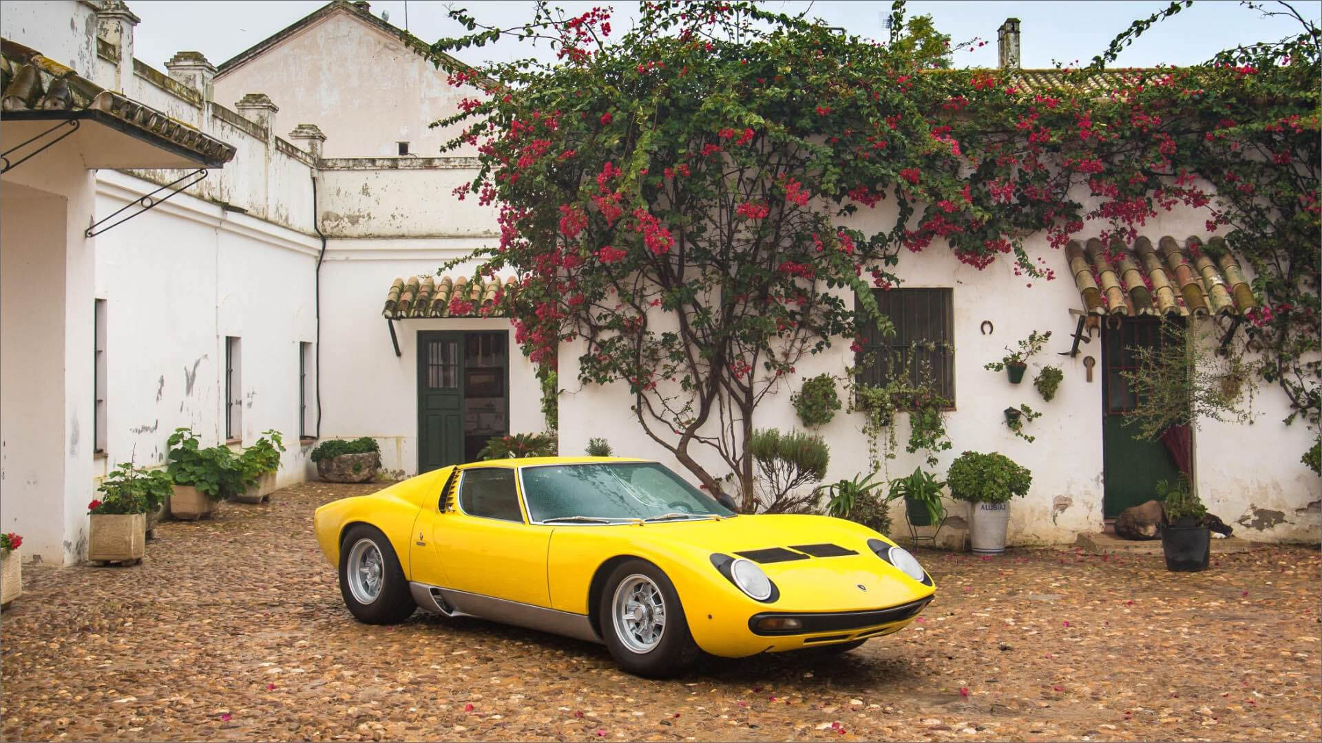 Lamborghini Miura color giallo parcheggiata davanti ad una casa con alberi e piante dietro