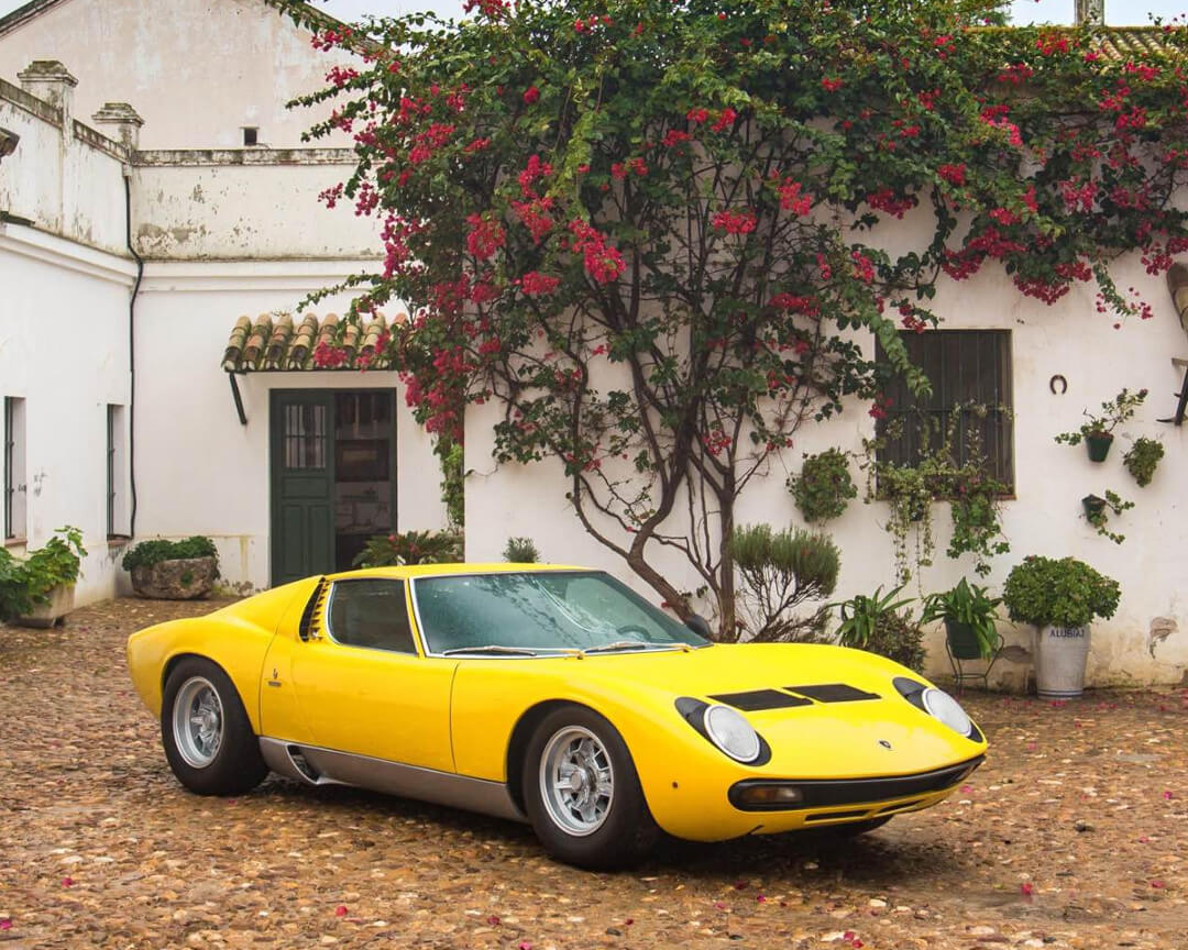 Lamborghini Miura color giallo parcheggiata davanti ad una casa con alberi e piante dietro