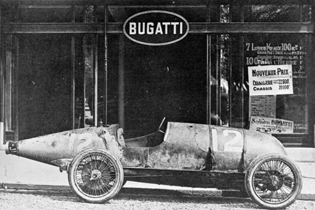 foto d'epoca in bianco e nero di un modello monoposto d'epoca marca Bugatti davanti al negozio con insegna Bugatti