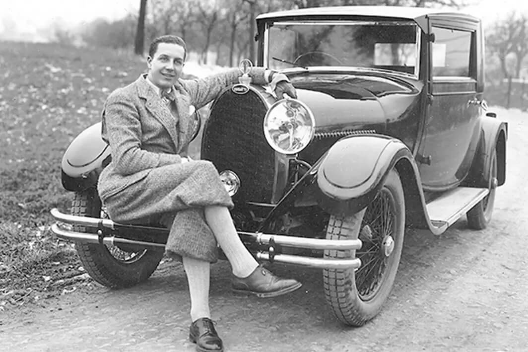 foto d'epoca in bianco e nero di Ettore Bugatti seduto su un modello di auto d'epoca marca Bugatti