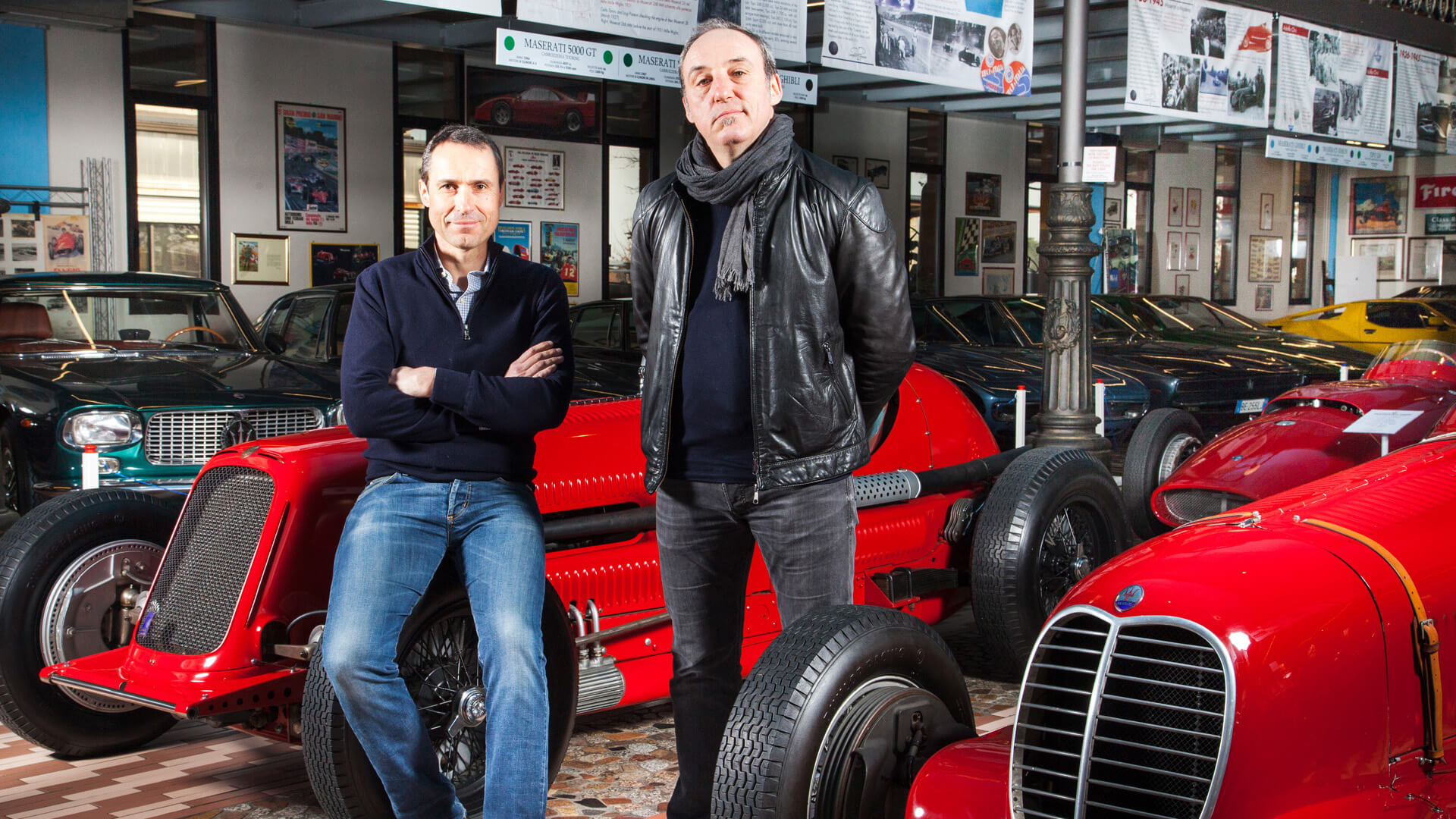 foto di Giovanni e Umberto Panini sorridenti con alle loro spalle la collezione di auto d'epoca