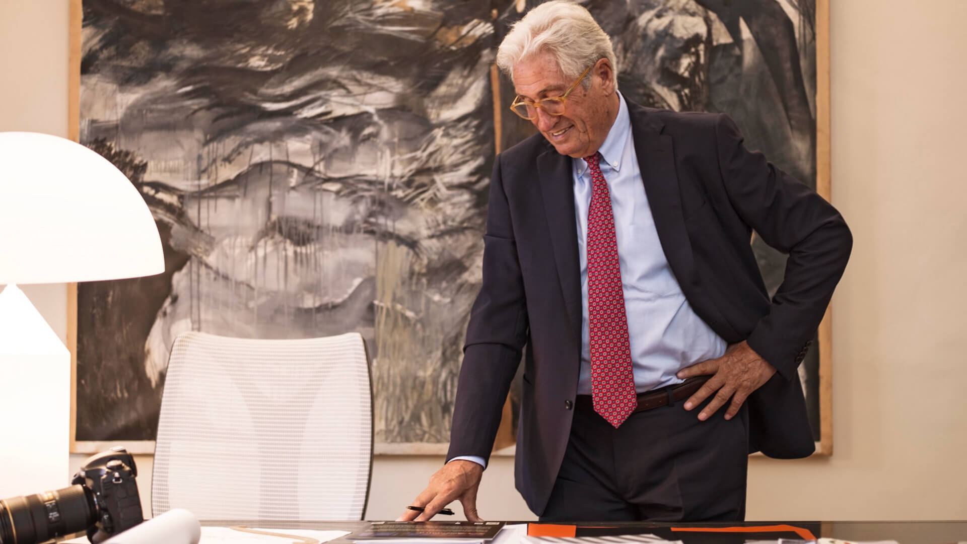 portrait of Giorgetto Giugiaro on his desk with lamp and artwork behind it