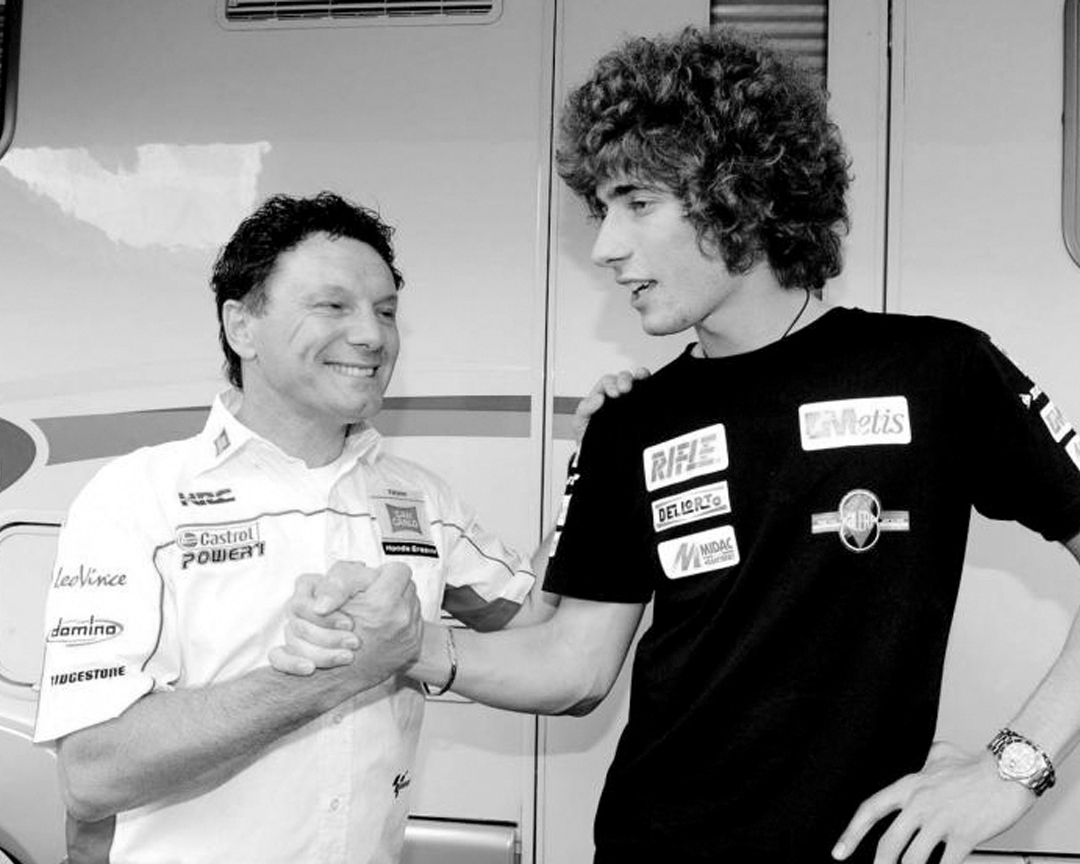Black and white photo of Fausto Gresini shaking hands with Marco Simoncelli
