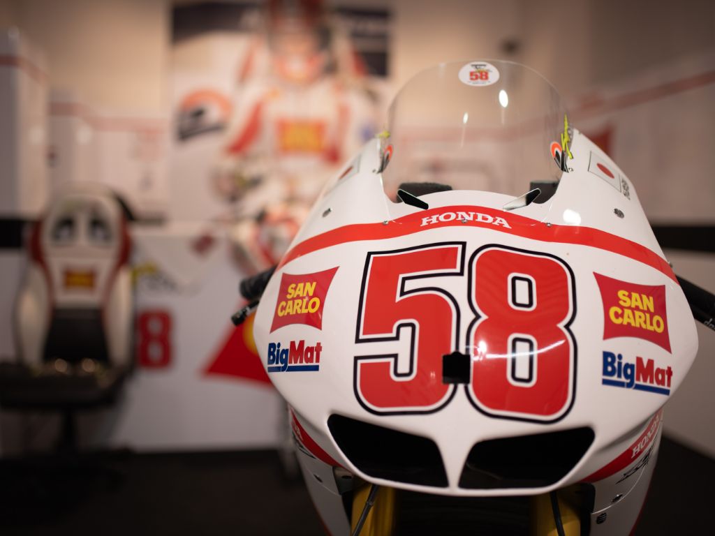Primo piano frontale del cupolino bianco di una moto da corsa Honda, caratterizzato dal grande numero 58 rosso e dai loghi degli sponsor San Carlo e BigMat.