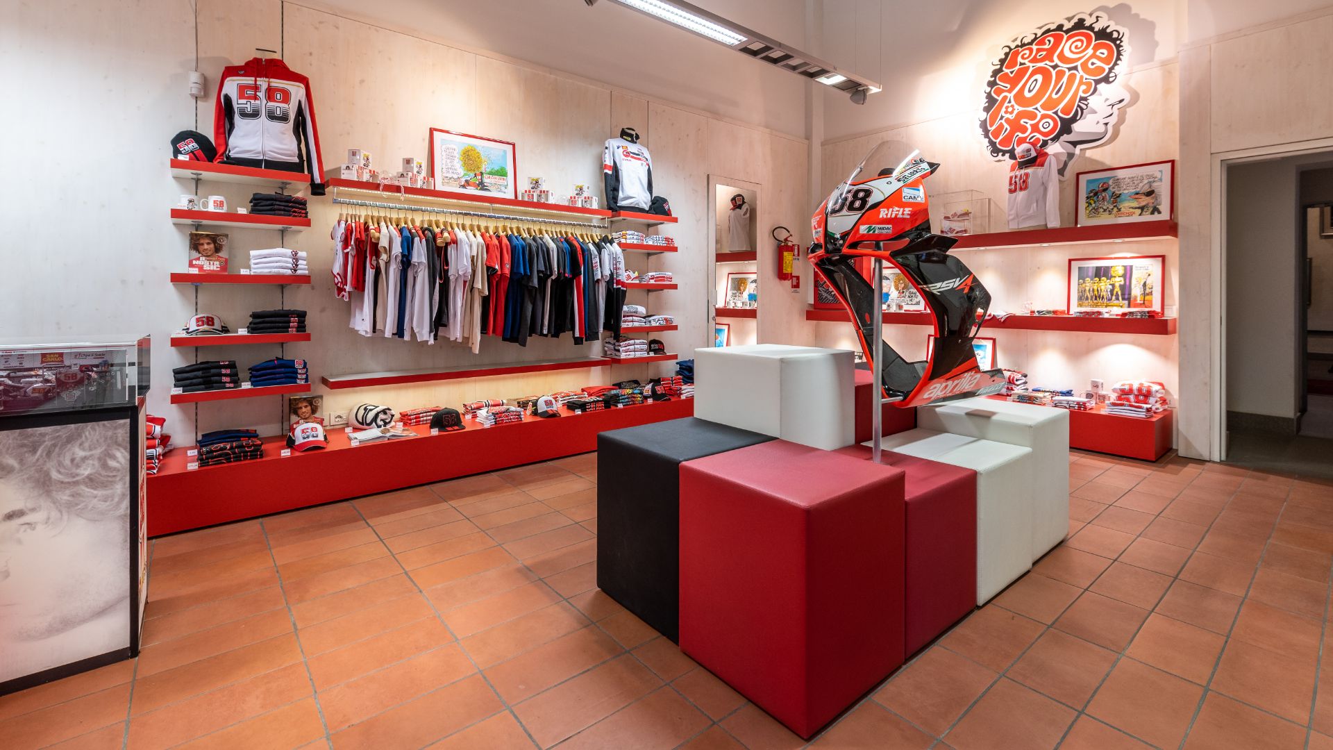L'interno del negozio di merchandising del museo, con scaffali pieni di abbigliamento e un'installazione centrale che espone la carena frontale numero 58 di una moto.