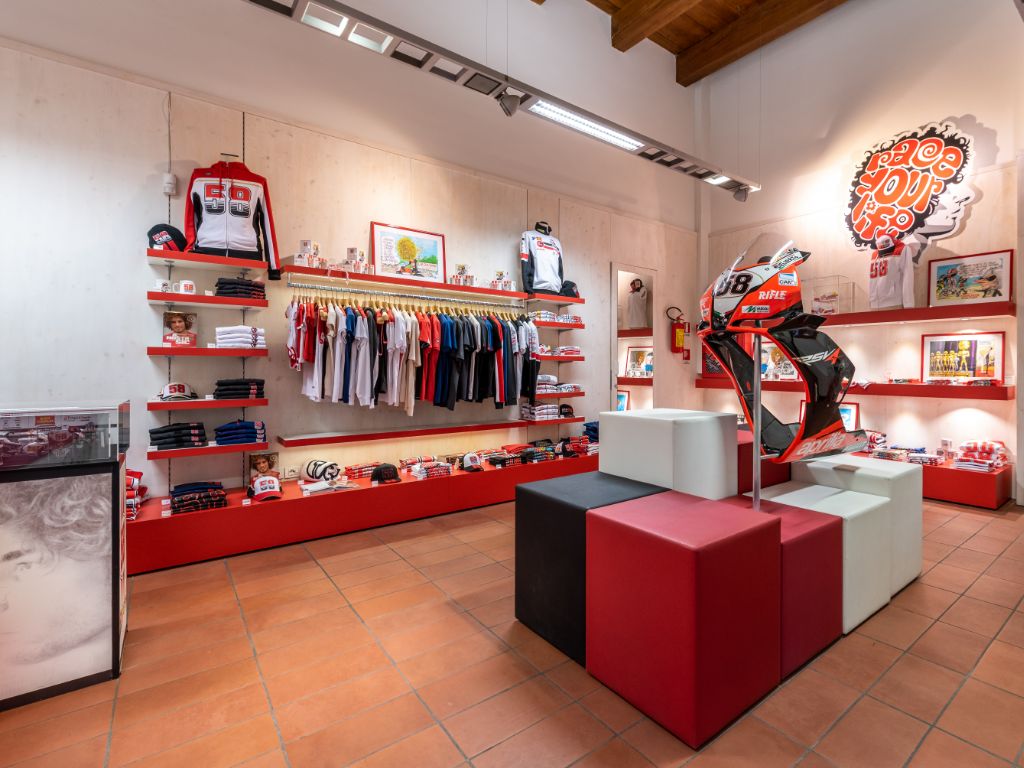 L'interno del negozio di merchandising del museo, con scaffali pieni di abbigliamento e un'installazione centrale che espone la carena frontale numero 58 di una moto.
