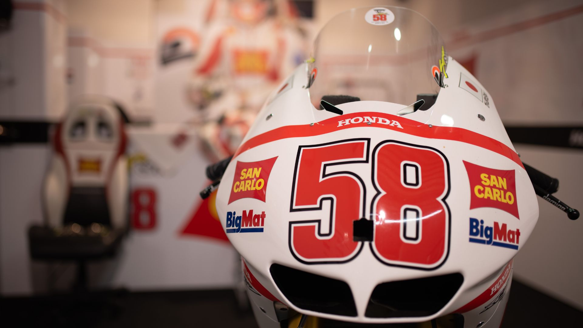 Primo piano frontale del cupolino bianco di una moto da corsa Honda, caratterizzato dal grande numero 58 rosso e dai loghi degli sponsor San Carlo e BigMat.