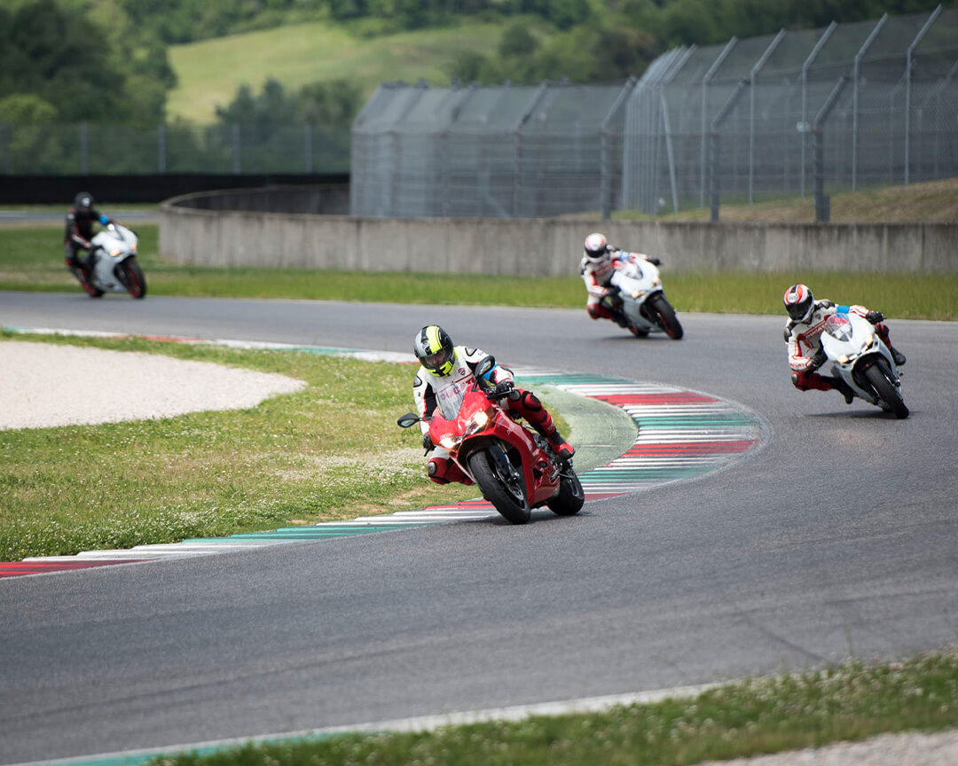 Red Ducati motorcycle followed by white Ducati motorcycles in circuit turn