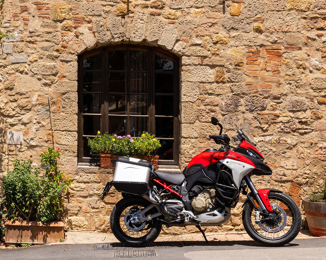 Side of a red Ducati Multistrada motorcycle on a wall of a country house in Tuscany