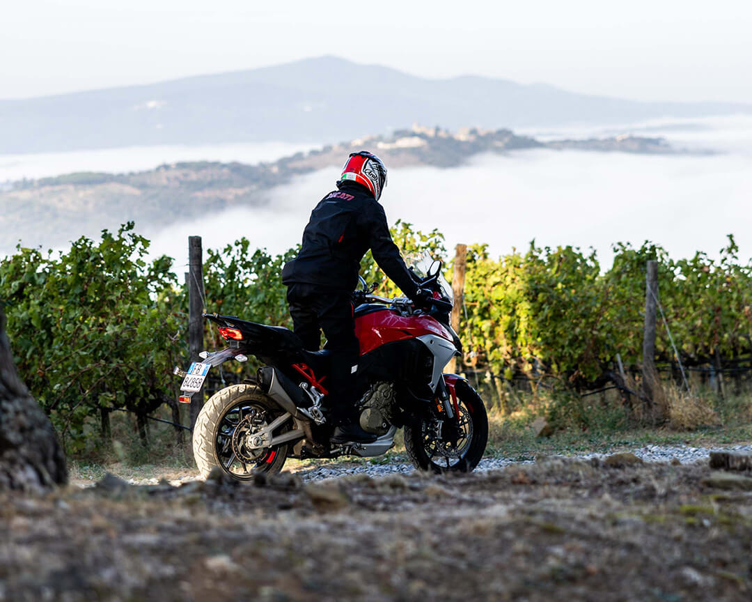Red ducati multistrada crossing a dirt road through the vineyards of Tuscany