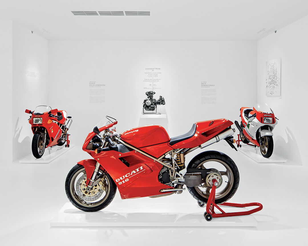 Ducati 916 rossa con altre due moto Ducati in una saletta bianca del museo