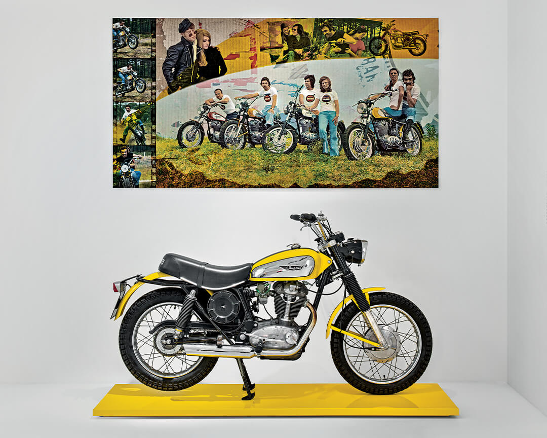 motocicletta scrambler ducati gialla degli anni 70 con poster pubblicitario dell'epoca esposta al Museo Ducati