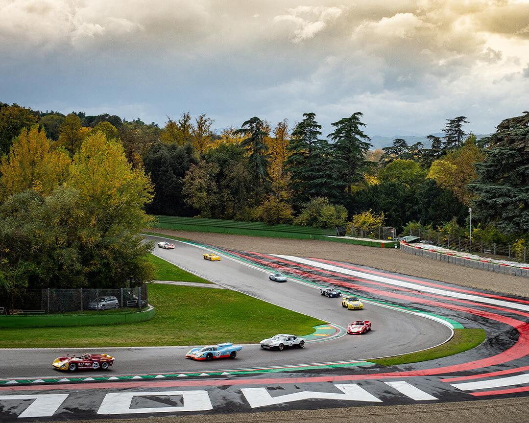 gara tra Porsche in curva con artwork Imola sul cordolo