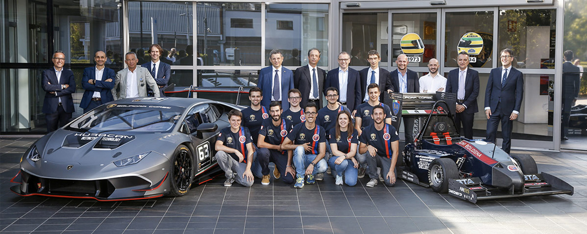 squadra di studenti con managers e docenti e una Lamborghini e il prototipo di un'auto da corsa