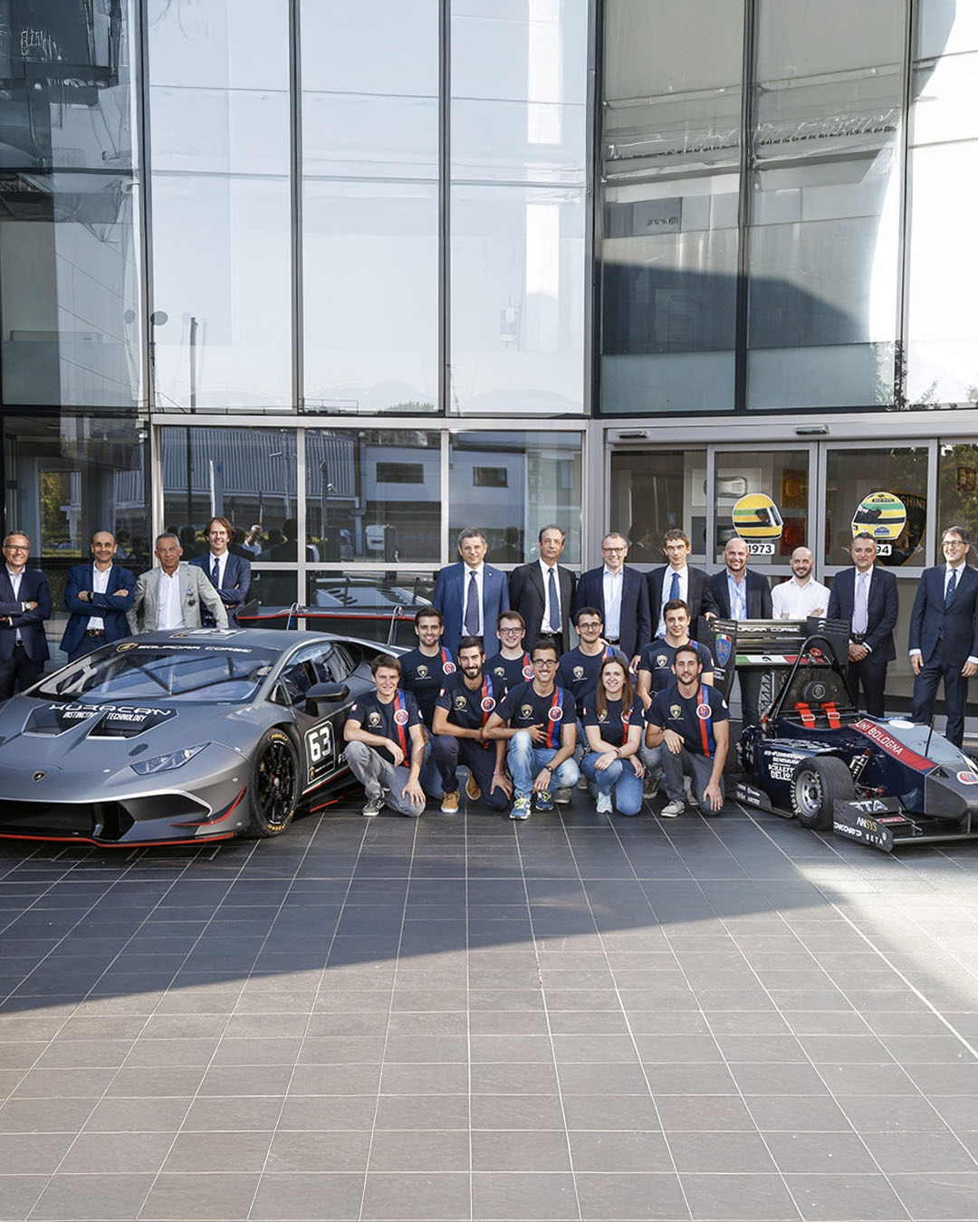 squadra di studenti con managers e docenti e una Lamborghini e il prototipo di un'auto da corsa