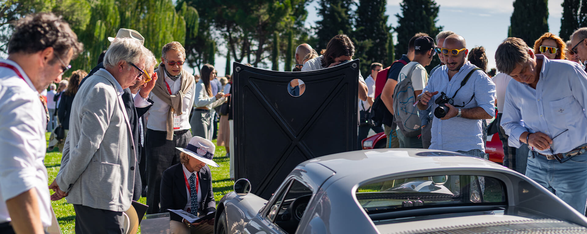 gruppo di appassionati attorno a una macchina d'epoca durante un evento all'aperto su prato