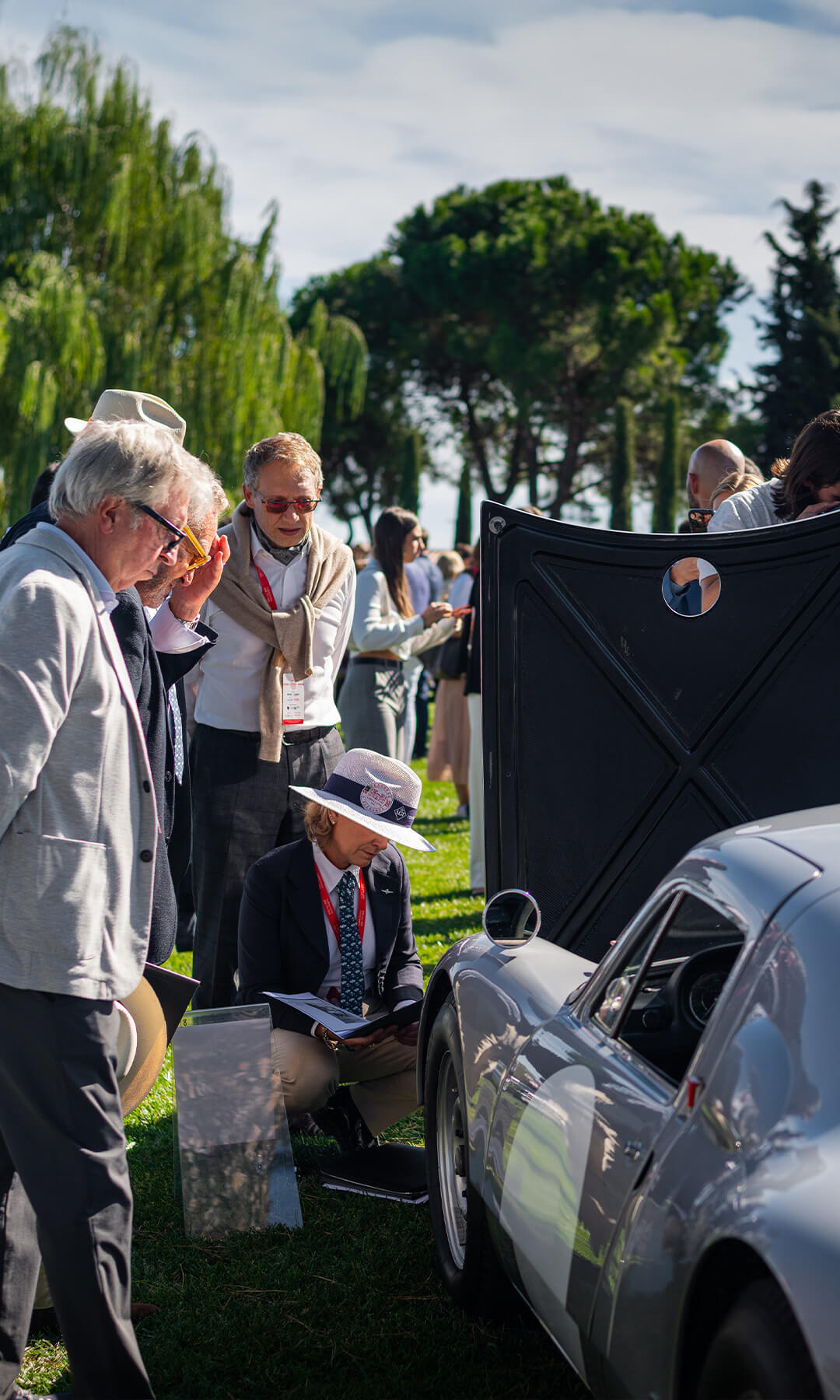 gruppo di appassionati attorno a una macchina d'epoca durante un evento all'aperto su prato